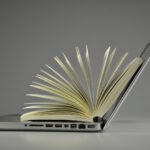 Aufgeklaptter Laptop mit auffächertem Buch