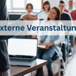 Im Hintergrund ist verschwommen eine Klasse mit erwachsenen menschen zu sehen. Vorne steht ein Dozent mit einem aufgeklappten Laptop auf dem Tisch.