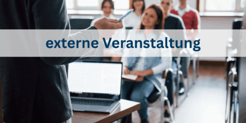 Im Hintergrund ist verschwommen eine Klasse mit erwachsenen menschen zu sehen. Vorne steht ein Dozent mit einem aufgeklappten Laptop auf dem Tisch.