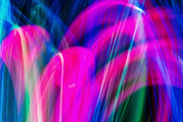 Das Bild zeigt eine bunte abstrakte Lichtmalerei. Es gibt keine erkennbaren Figuren oder Gegenstände. Stattdessen sieht man geschwungene Linien und Bögen in leuchtenden Farben: Pink / Magenta dominiert das Bild mit kräftigen Bögen. Blau ist stark im Hintergrund und an den Rändern zu sehen. Grün erscheint als einzelne vertikale und geschwungene Linien dazwischen. Stellenweise mischen sich die Farben ineinander, sodass fließende Übergänge entstehen. Das Bild wirkt lebendig, dynamisch und erinnert an eine Lichtshow, Neonfarben oder lange Belichtungszeiten bei bewegtem Licht.