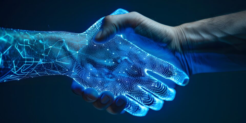 Eine menschliche Hand schüttelt eine künstliche, digital dargestellte Hand. Die digitale Hand besteht aus leuchtenden, blauen Linien und Punkten, die an ein Netzwerk oder ein Schaltkreisdiagramm erinnern. Die Szene ist dunkel gehalten, der Fokus liegt auf dem Handschlag und dem Kontrast zwischen organischer und digitaler Struktur.